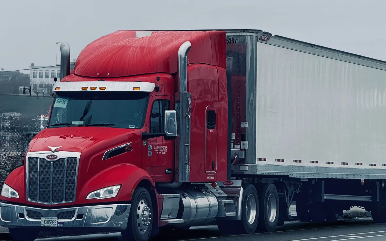 Red semi truck pulling a white trailer down a highway